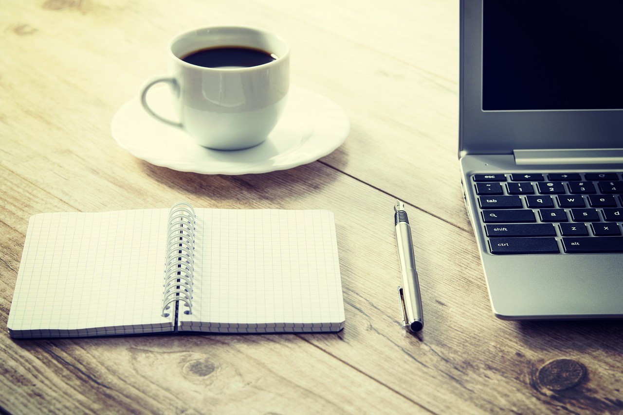 writing notebook with laptop and coffee next to it